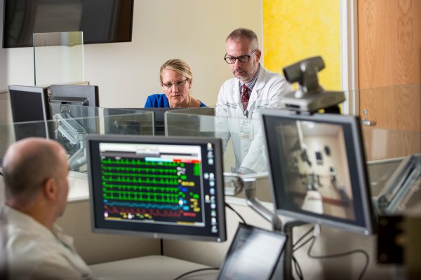 Mark Pippy (foreground), Michelle Buck, and Kevin Curtis work with a remote bedside team to monitor a patient's vital signs in DHMC's Connected Care Center for Telehealth. Photo by Mark Washburn